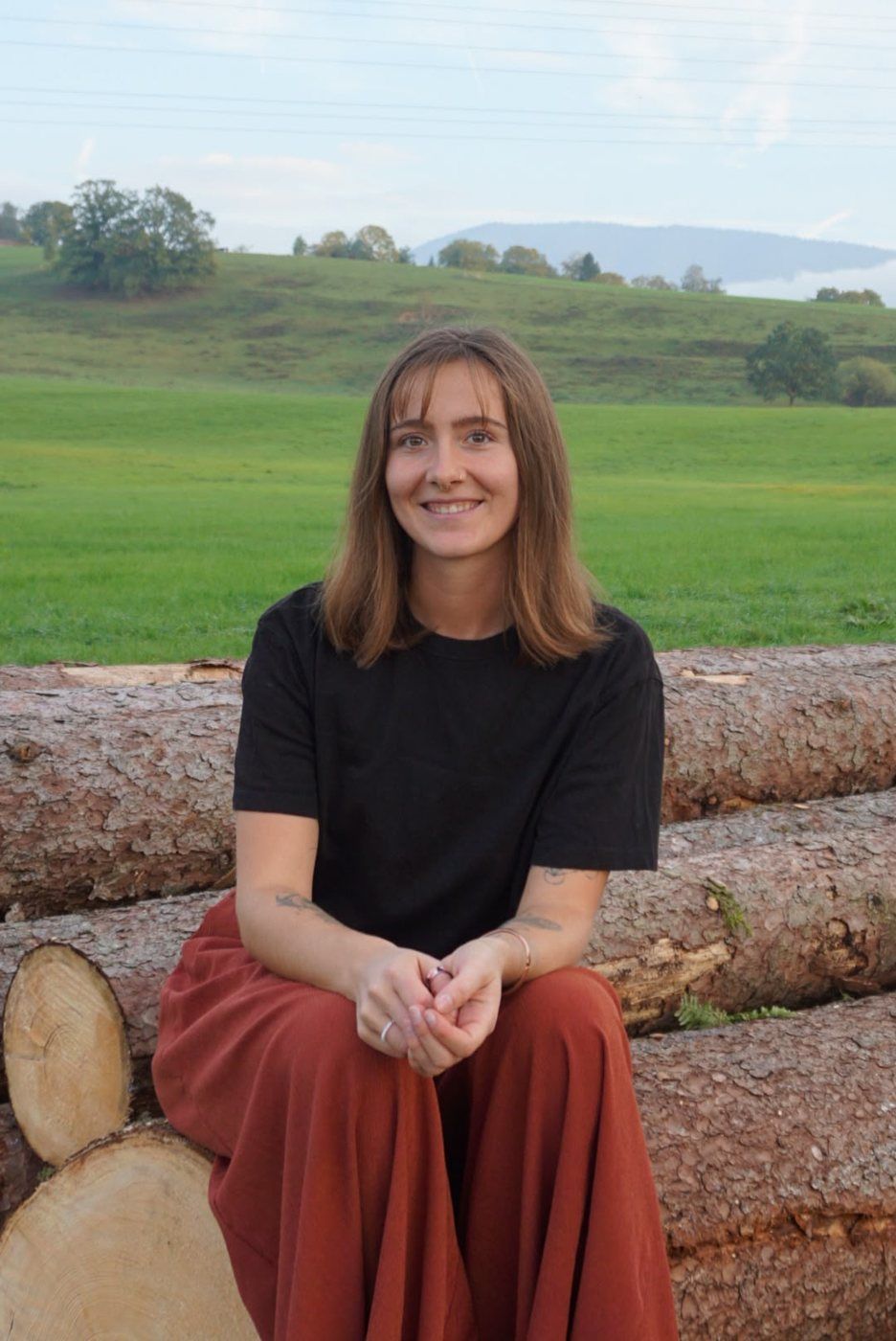 Johanna Bernrieder sitzt lächelnd auf Baumstämmen vor einer grünen Wiese