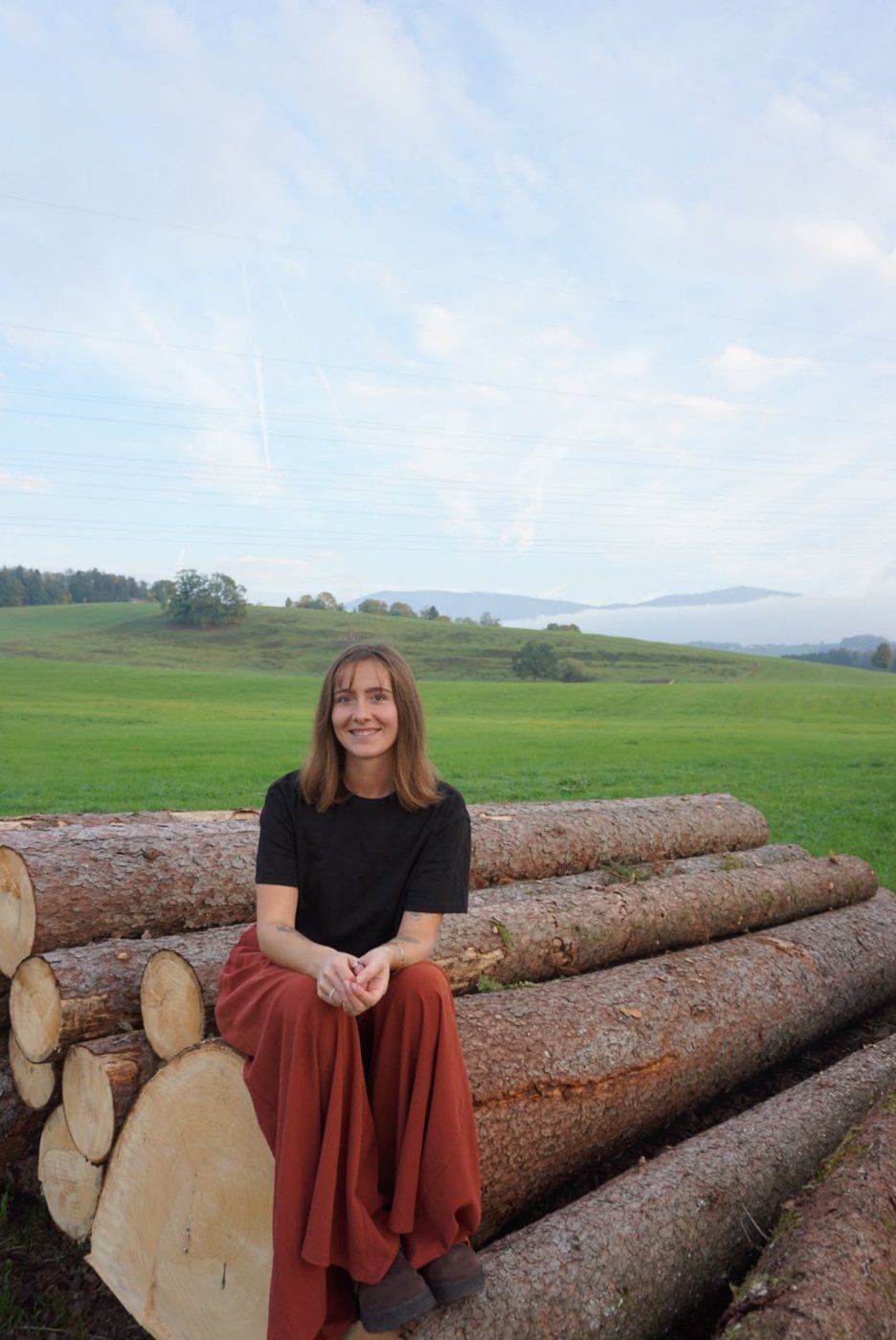 Johanna Bernrieder auf Baumstämmen, im Hintergrund Wiesen und Berge